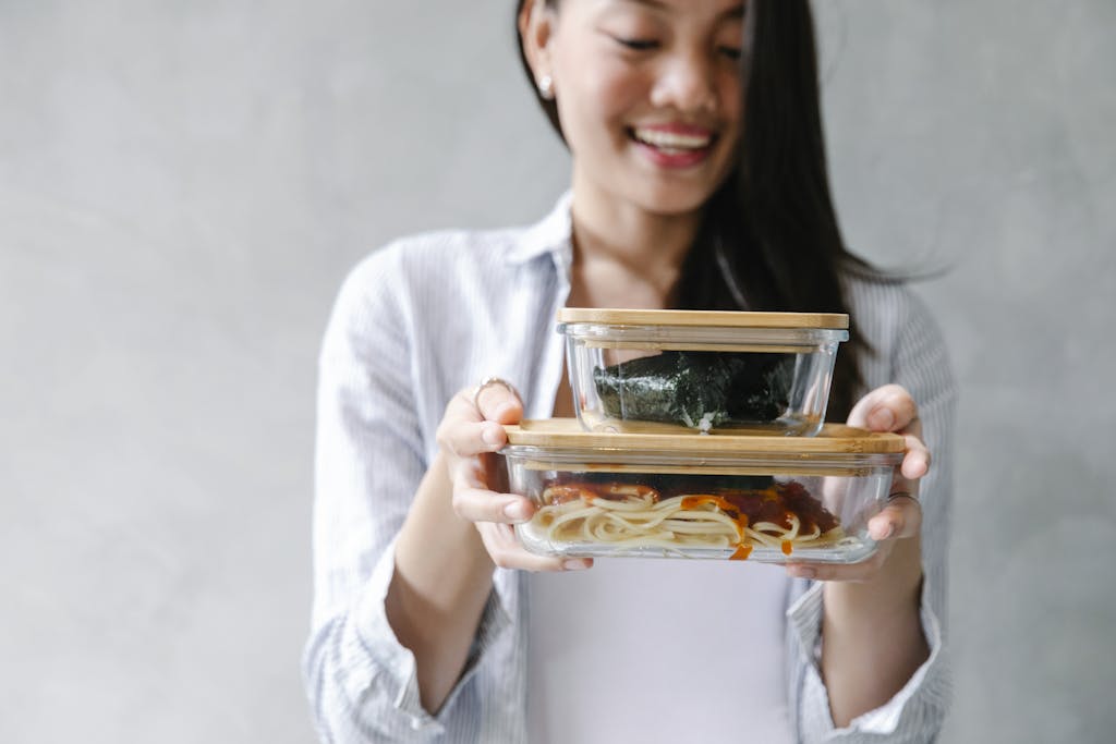 Smiling Asian woman holding two bento boxes filled with delicious food indoors.